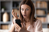 Close up young shocked woman looking at mobile phone screen.