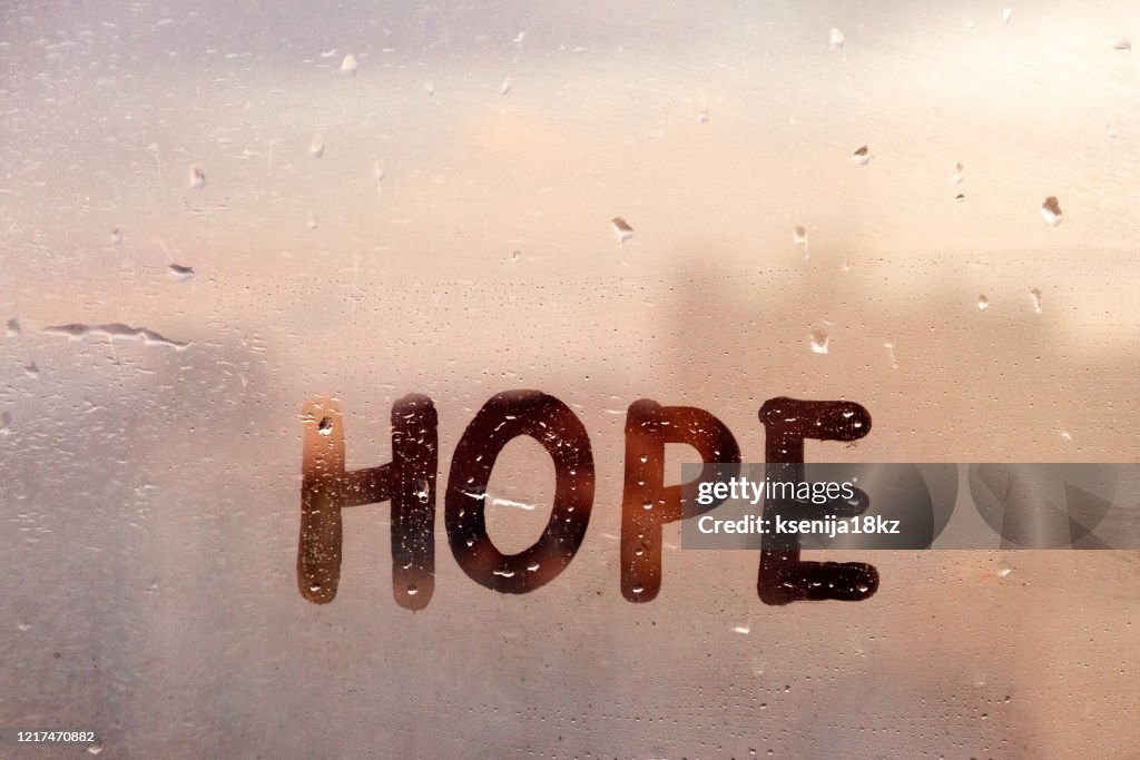 Foggy glass on window with written finger word yellow color Hope concept photo with copy space on blue and warm background