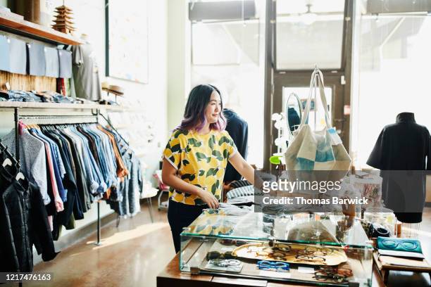 smiling shopkeeper organizing display in boutique - women wearing see through clothing stockfoto's en -beelden