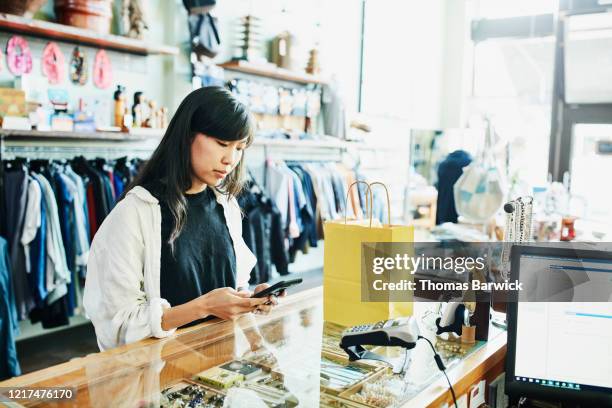 woman using smart phone to pay for purchase in clothing boutique - smartphones dangling stock pictures, royalty-free photos & images