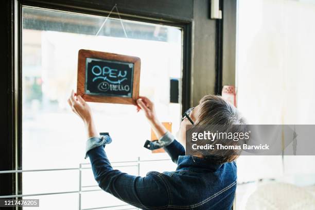 senior female business owner turning open sign on door before opening boutique - small business stock pictures, royalty-free photos & images