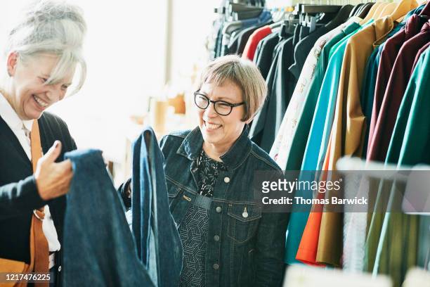 smiling senior female shop owner helping client pick out outfit in boutique - women in transparent clothing - fotografias e filmes do acervo