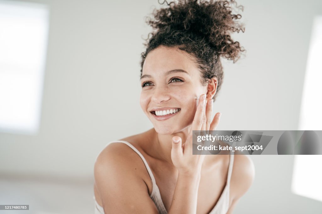 Smiling young women applying moisturiser to her face