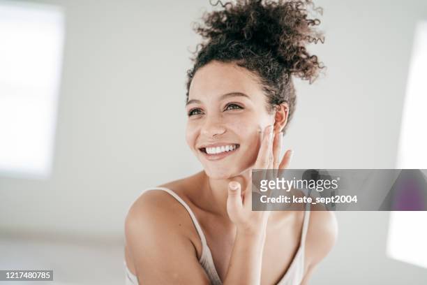 smiling young women applying moisturiser to her face - glowing stock pictures, royalty-free photos & images