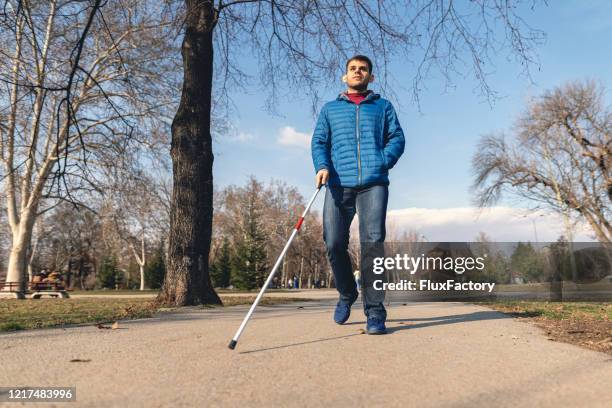 junger mann mit sehbehinderung zu fuß mit hilfe eines gehstockes - blindness stock-fotos und bilder