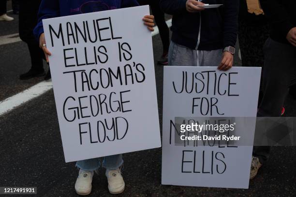 People hold signs during a vigil for Manuel Ellis, a black man whose March death while in Tacoma Police custody was recently found to be a homicide,...