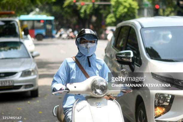 Woman, wearing protective clothing to shield from the sun, rides a scooter as the temperature soars in Hanoi on June 4, 2020.
