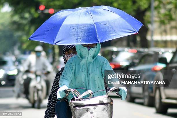 People, wearing protective clothing to shield from the sun, ride a bicycle as the temperature soars in Hanoi on June 4, 2020.