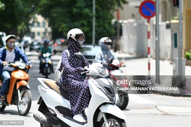 Woman , wearing protective clothing to shield from the sun, rides a scooter as the temperature soars in Hanoi on June 4, 2020.