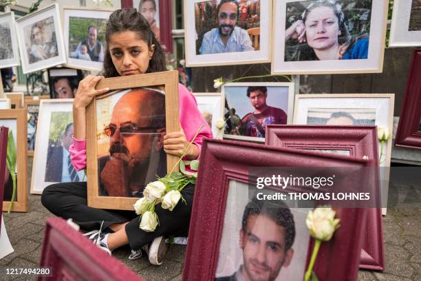 Syrian campaigner Wafa Mustafa sits between pictures of victims of the Syrian regime as she holds a picture of her father, during a protest outside...