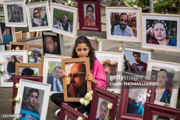 Syrian campaigner Wafa Mustafa sits between pictures of victims of the Syrian regime as she holds a picture of her father, during a protest outside...