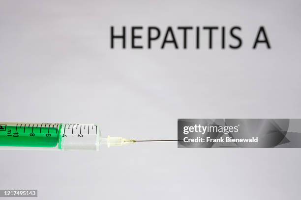 This photo illustration shows a disposable syringe with hypodermic needle, HEPATITIS A written on a white board behind.