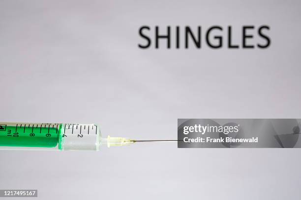 This photo illustration shows a disposable syringe with hypodermic needle, SHINGLES written on a white board behind.