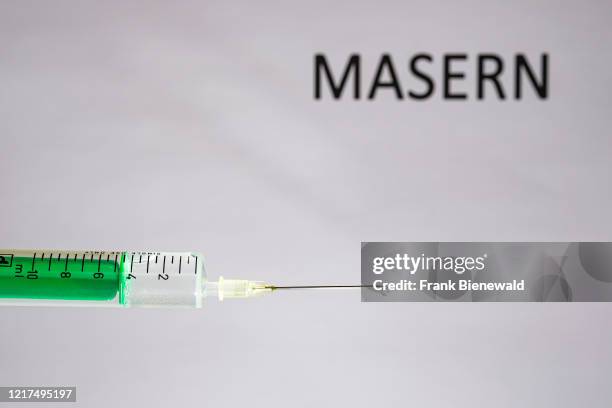 This photo illustration shows a disposable syringe with hypodermic needle, MASERN written on a white board behind.