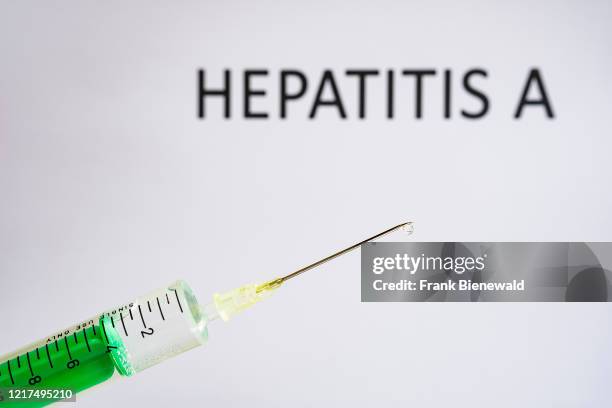 This photo illustration shows a disposable syringe with hypodermic needle, HEPATITIS A written on a white board behind.