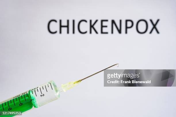 This photo illustration shows a disposable syringe with hypodermic needle, CHICKENPOX written on a white board behind.