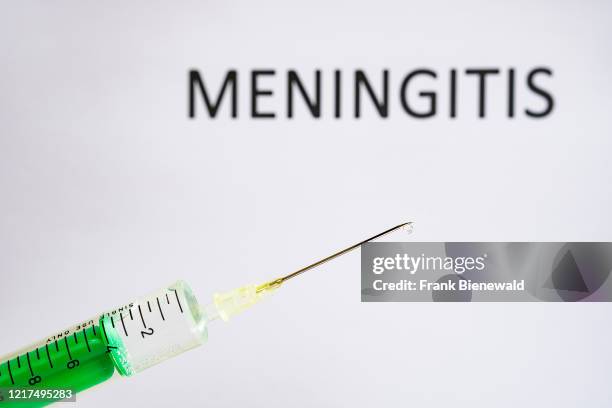 This photo illustration shows a disposable syringe with hypodermic needle, MENINGITIS written on a white board behind.