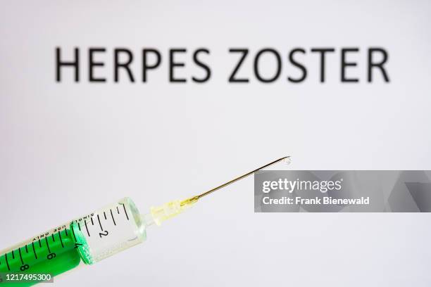 This photo illustration shows a disposable syringe with hypodermic needle, HERPES ZOSTER written on a white board behind.