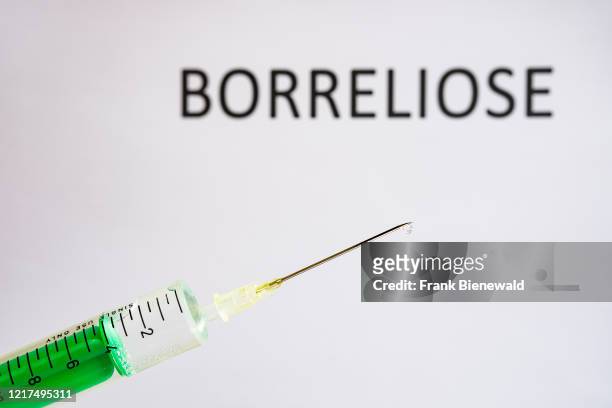 This photo illustration shows a disposable syringe with hypodermic needle, BORRELIOSE written on a white board behind.