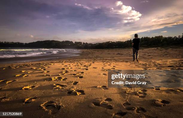 Woman walks near footprints left in the sand by fellow walkers at Narrawallee Beach at sunset on April 2, 2020 in Mollymook, Australia. Public...