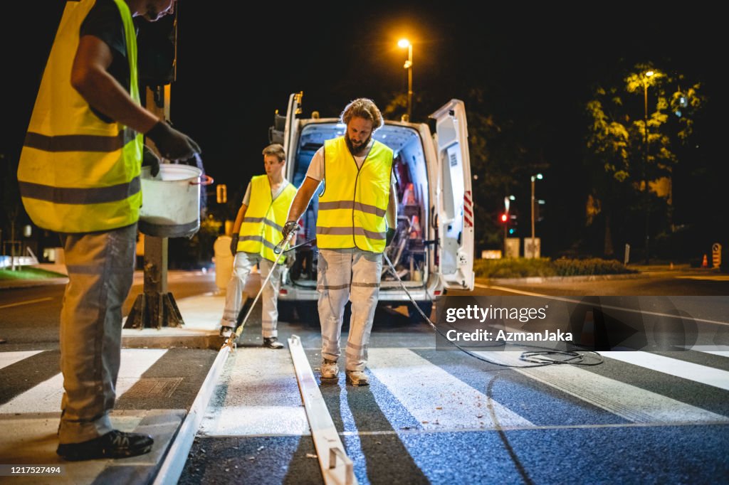 Construction Crew Spray Painting Crosswalk Stripes at Night