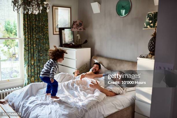 gay couple waking up with young son jumping on bed - jumping on bed stockfoto's en -beelden