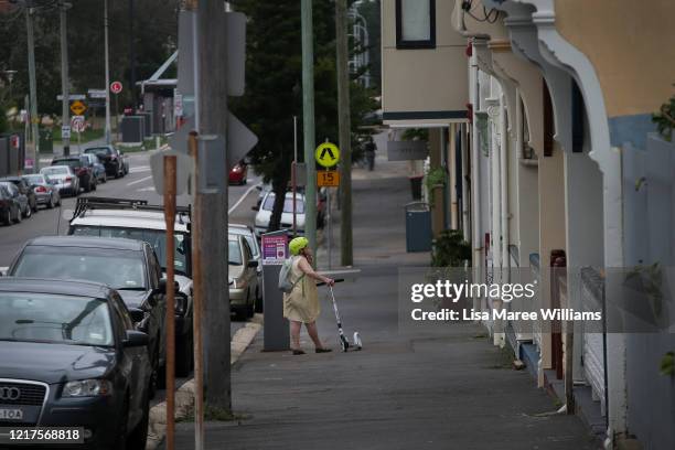 Woman stands with her scooter on a quiet street on April 08, 2020 in Newcastle, Australia. Public gatherings are now limited to two people, while...