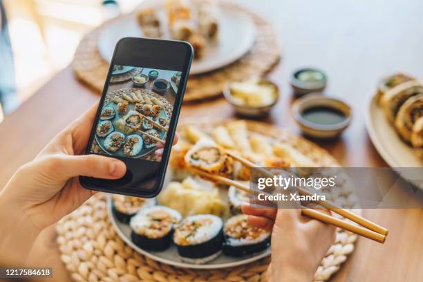 frau macht foto von maki sushi mit smartphone - woman sushi stock-fotos und bilder