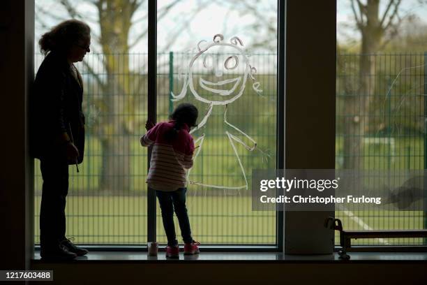 Young girl paints a picture of herself on the school window as children of key workers take part in school activities at Oldfield Brow Primary School...