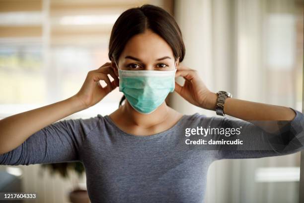 portrait of young woman putting on a protective mask for coronavirus isolation - protective face mask stock pictures, royalty-free photos & images