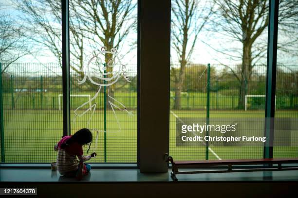 Young girl paints a picture of herself on the school window as children of key workers take part in school activities at Oldfield Brow Primary School...