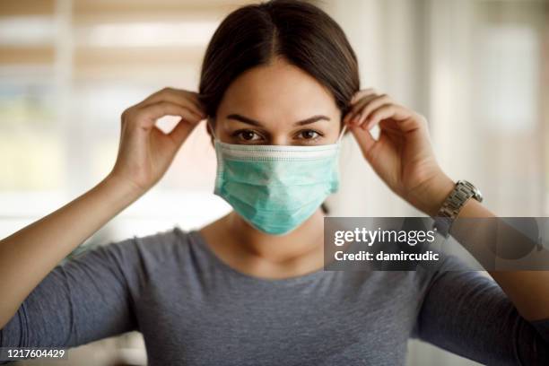 portrait of young woman putting on a protective mask - mask imagens e fotografias de stock