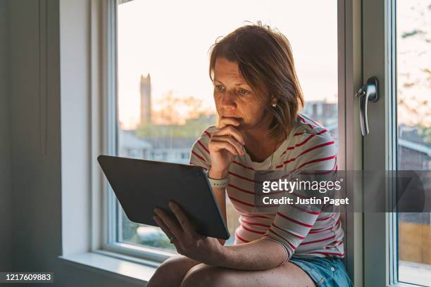 woman using digital tablet on window sill - pandemic illness stock pictures, royalty-free photos & images