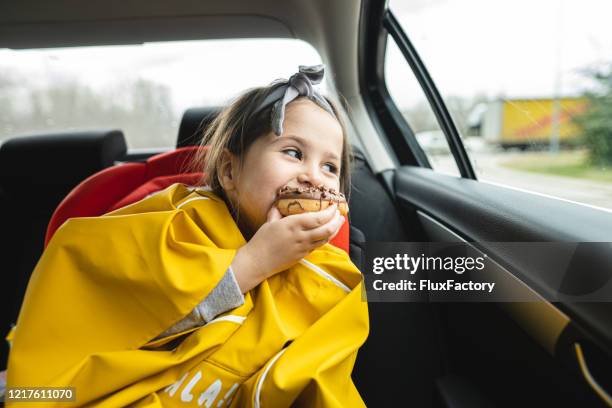 mooi kind dat een donut eet terwijl het kijken door een autovenster - eating donuts stockfoto's en -beelden