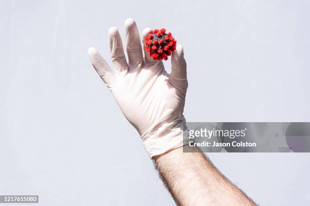 man's hand wearing a white protective glove, holding a coronavirus model - malattia infettiva foto e immagini stock