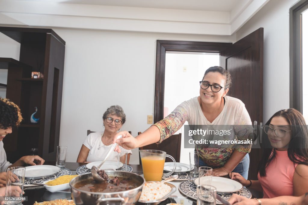 Family having lunch at dining table served with feijoada, typical brazilian black bean stew