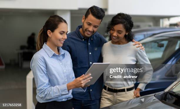 verkäuferin in einem autohaus im gespräch mit einem glücklichen paar - customer service documents stock-fotos und bilder