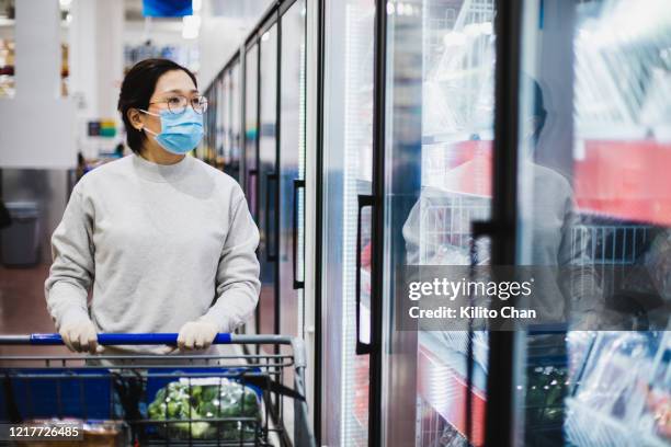 asian female wearing a face mask shopping at the supermarket - covid shopping stock pictures, royalty-free photos & images