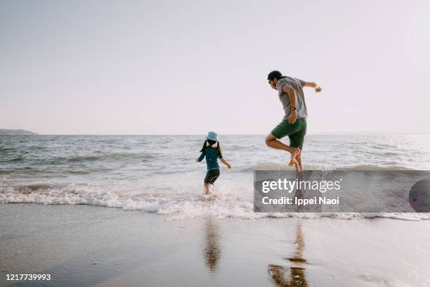 rear view of father and child jumping on beach - beach family jumping stock pictures, royalty-free photos & images