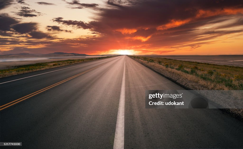 Straight asphalt road running to the horizon at sunset