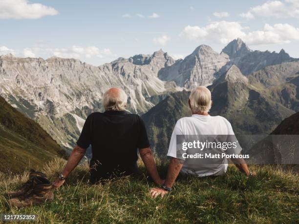 two seniors hikers sit and admire the view - paar in sportkleidung stock-fotos und bilder