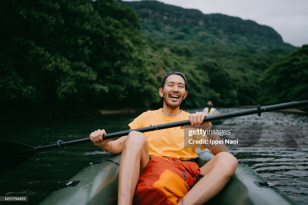 Man paddling kayak in mangrove river and laughing, Iriomote, Japan