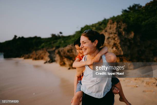 mother giving little girl piggyback ride on beach, okinawa, japan - océano pacífico fotografías e imágenes de stock