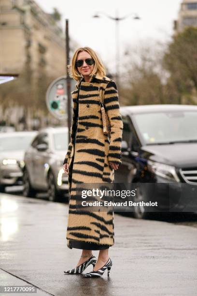 Lisa Aiken wears sunglasses, a brown and black zebra pattern printed long coat, a black dress, black and white zebra pointy shoes, a golden metallic...