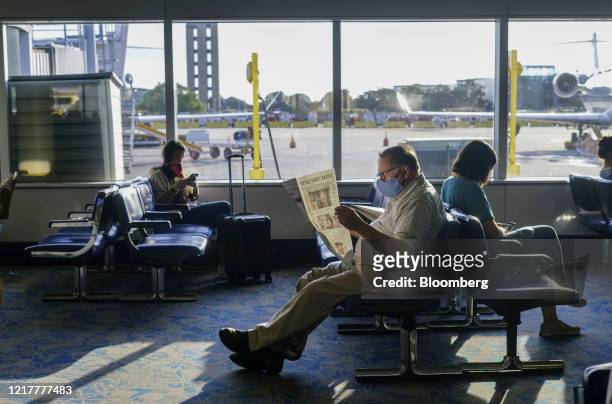 Traveler wearing a protective mask reads a newspaper while sitting at a gate at the Charlotte Douglas International Airport in Charlotte, North...