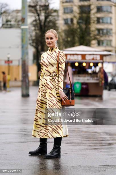 Thora Valdimars wears silver metallic earrings, a yellow and brown zebra pattern printed dress, a black and brown leather bag from Loewe, black...