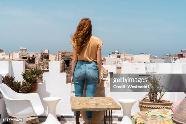 back view of young woman standing on roof terrace looking at distance, essaouira, morocco - essaouira photos et images de collection