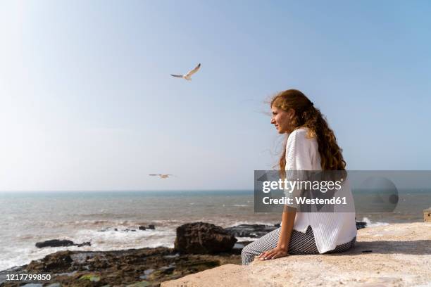 young woman enjoying sunlight near the sea, essaouira, morocco - essaouira photos et images de collection