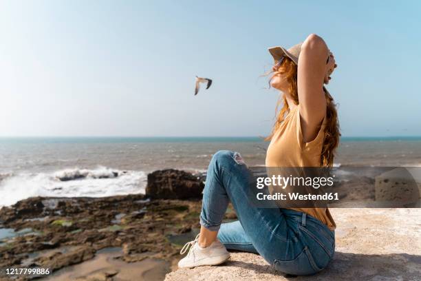 young woman enjoying sunlight near the sea, essaouira, morocco - essaouira photos et images de collection