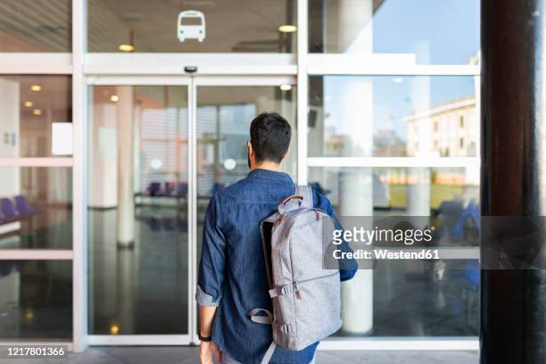 back view of man with backpack in front of entrance of bus station - sliding door stock-fotos und bilder